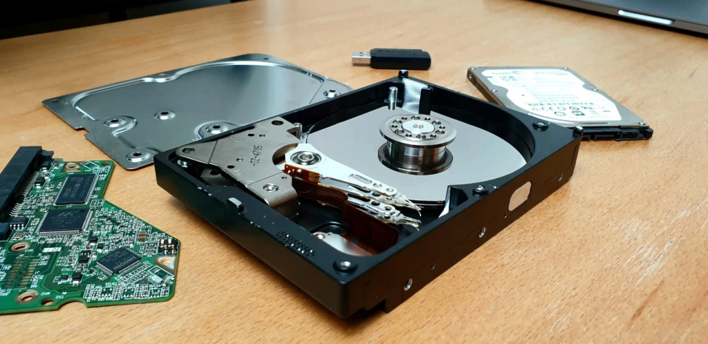 Un disque dur ouvert est posé sur une table, avec une clé USB en arrière-plan. L'objectif de cette image est d'attirer l'attention sur le thème de la récupération de données.