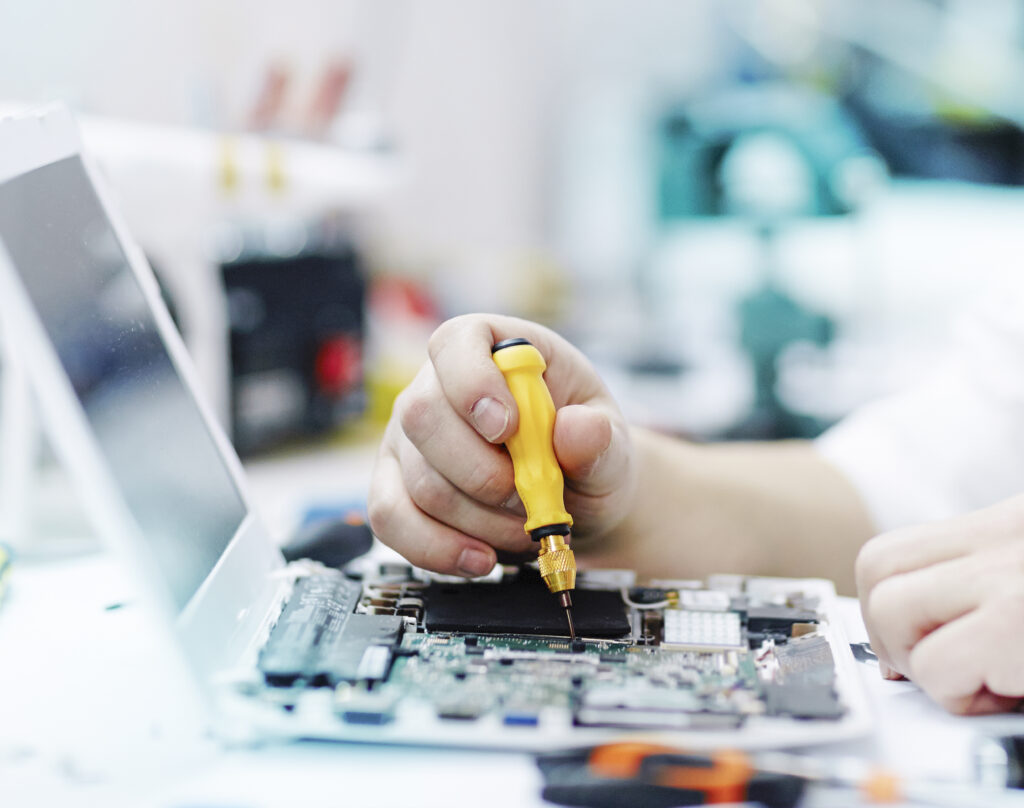 Person in the atelier unscrews screws in an open laptop with a screwdriver