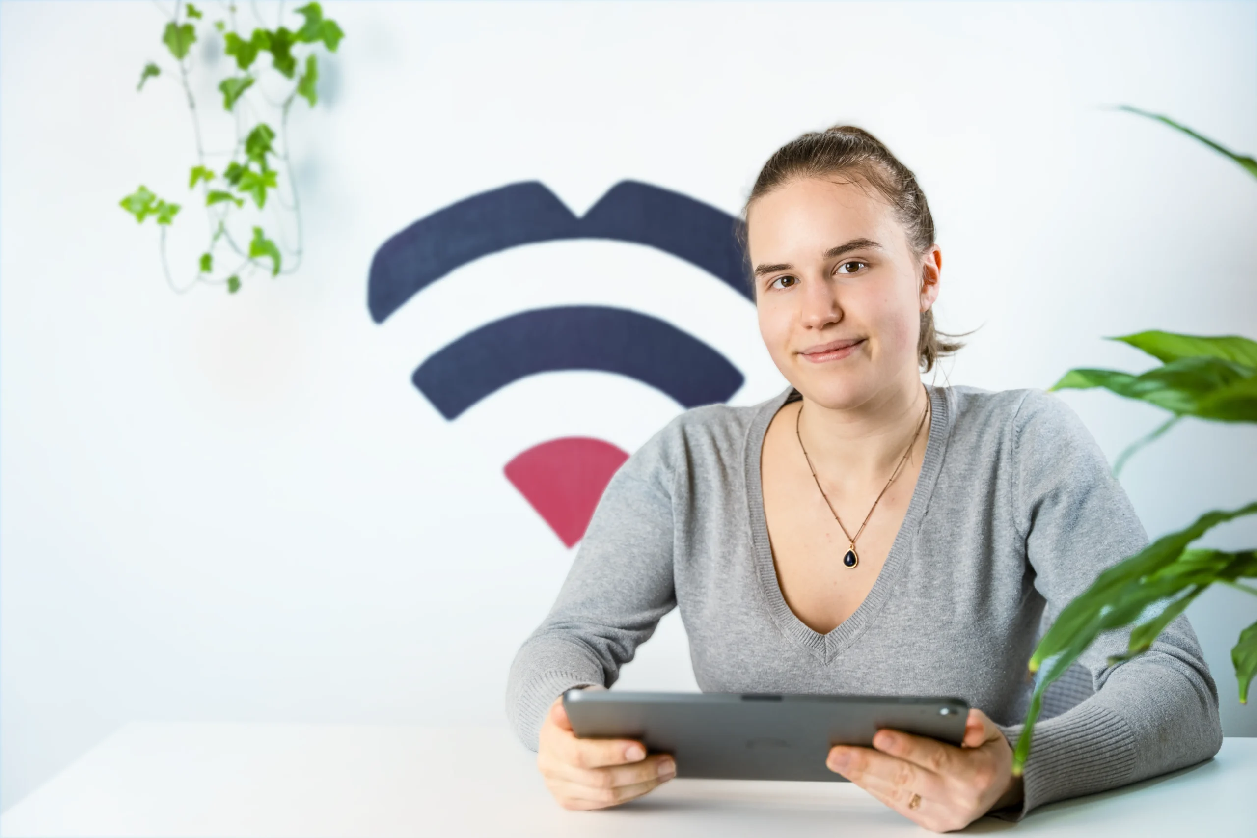 IT-Dokter employee at the reception desk with iPad surrounded by plants, in the background you can see the IT-Dokter logo