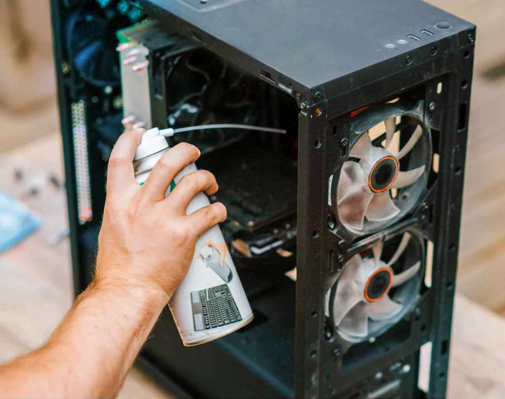 ein Mann benutzt Druckluft-Spray zum Putzen des offenes Computers im Atelier