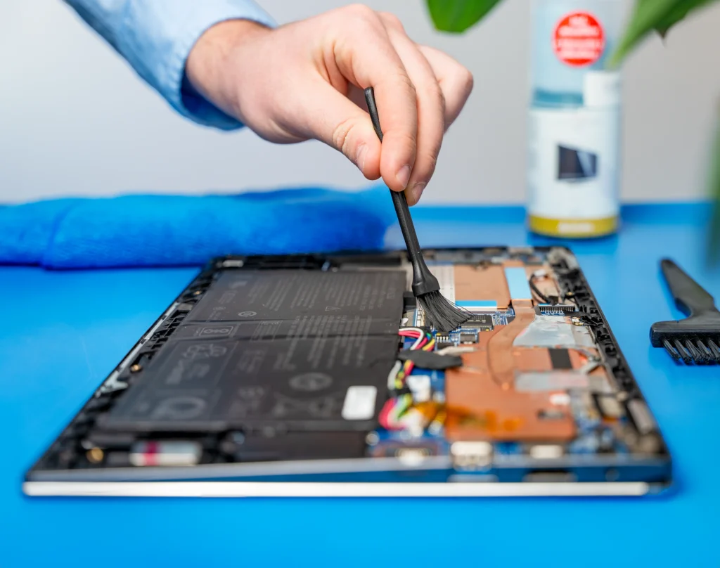 Cleaning an open laptop with a brush and various cleaning utensils on the table