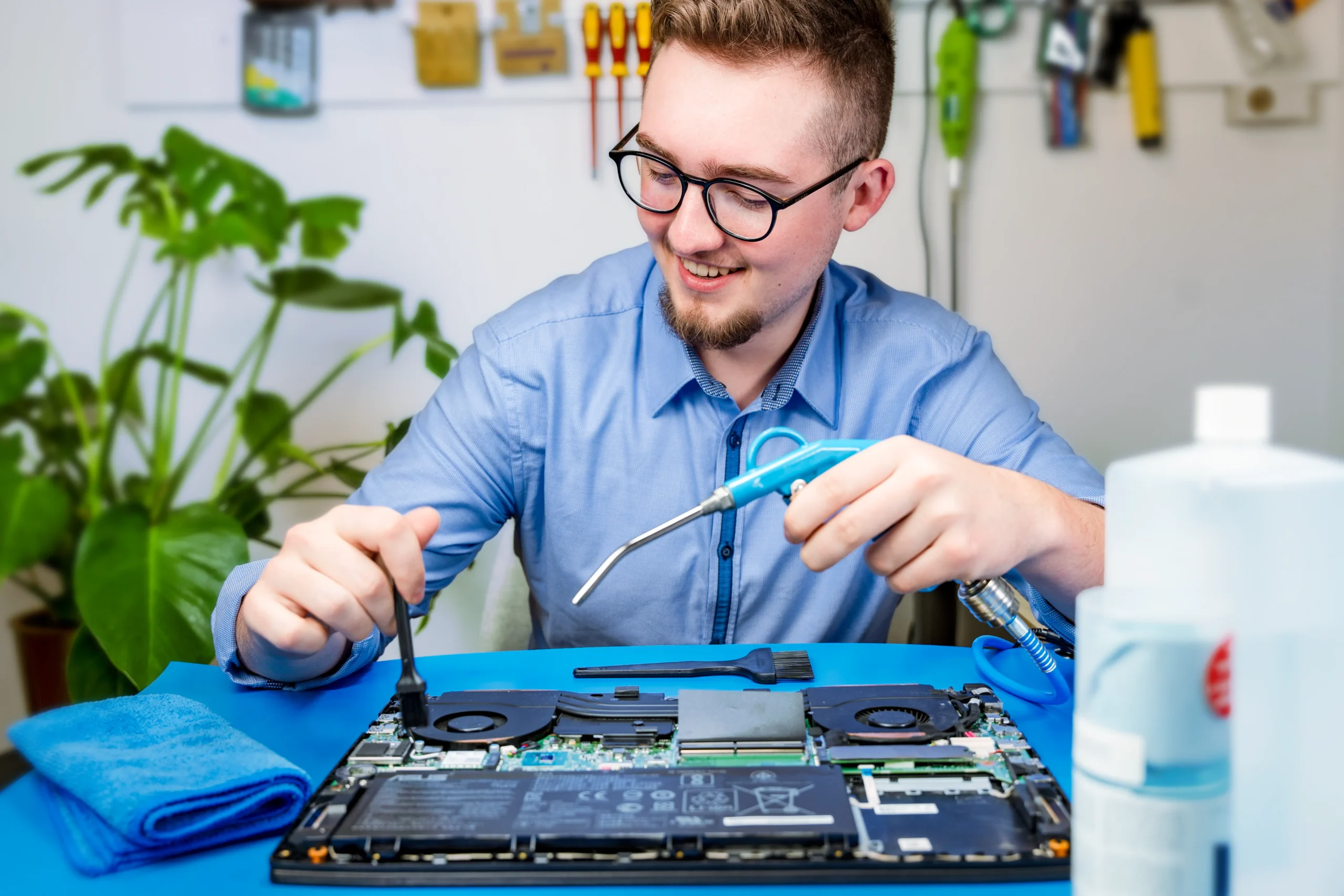 smiling IT doctor technician cleaning a laptop with a brush and compressor gun